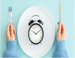 person's hands holding fork and knife next to plate with an alarm clock in the center