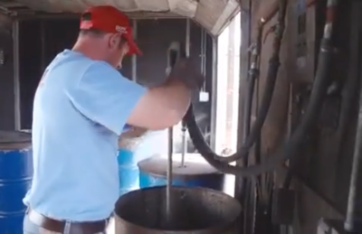 A person in a red hat holding a hose going into the steam boiler barrels